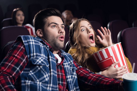 Two people watching a scary movie at theater.