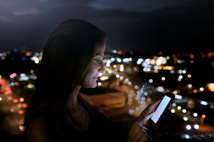 Person looking at their phone with a digital face looking back at them.