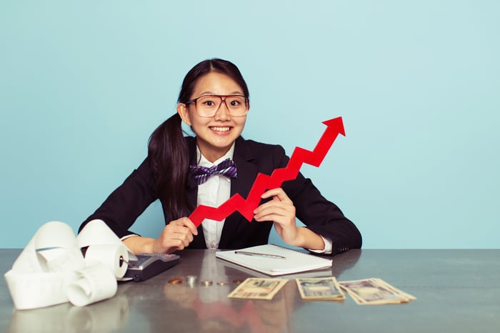 Child at a desk with money, a calculator, and upward-pointing arrow.