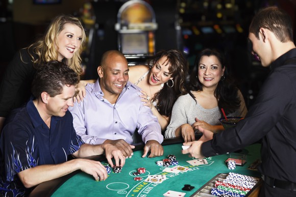 Five people at a casino table with an employee dealing cards.