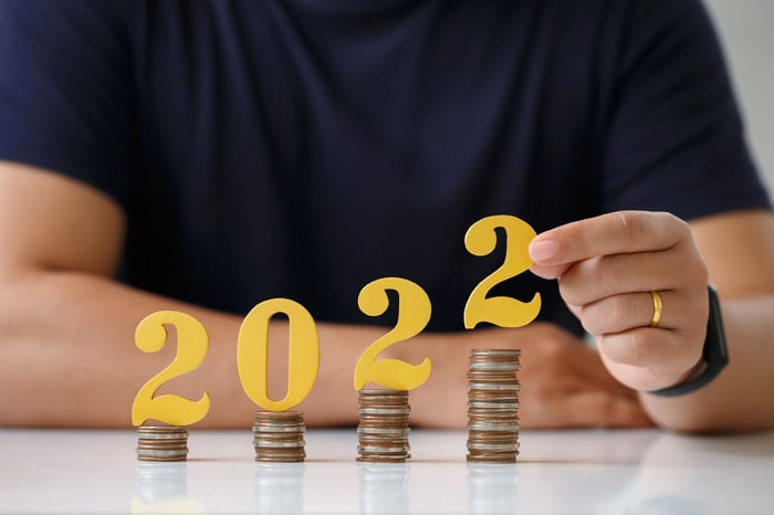 A person stacking '2022' on increasing stacks of coins.