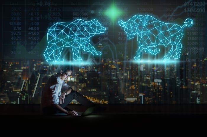 Person looking at a laptop screen while sitting under a virtual Bear versus Bull. 