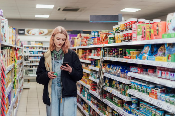 A person looking at a phone in the food aisle of a store.