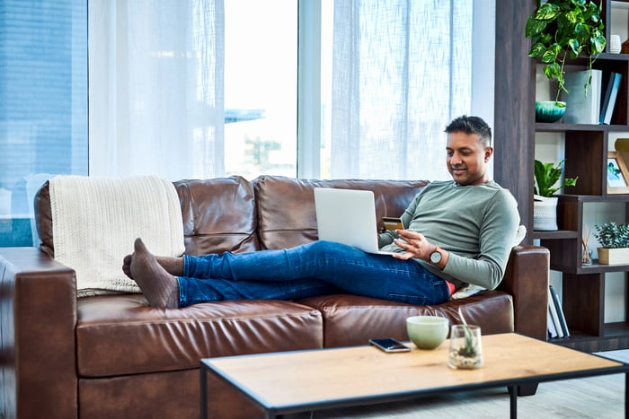 A person on a couch with a laptop and a credit card in hand.