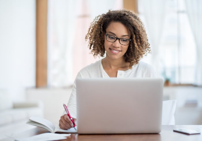 A person at a laptop writing in a notebook.