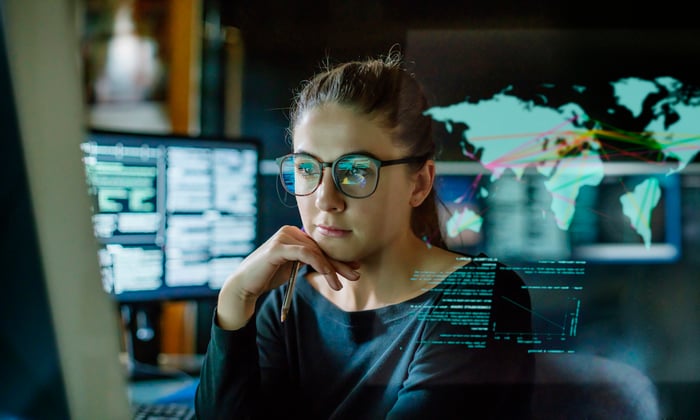 A person in a darkened office looking at charts and graphs on a computer monitor.