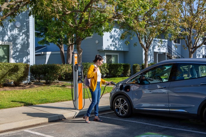 Person charging car outside apartment building. 