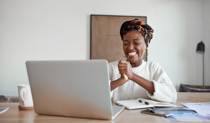 A person sitting at a table, looking at a computer, and smiling.