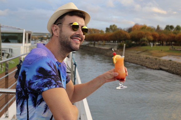 Tourist on a cruise ship holding a fruity drink by the railing.