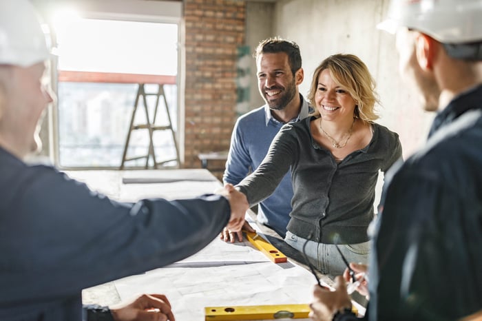 Smiling people shake hands at a homebuilding worksite.