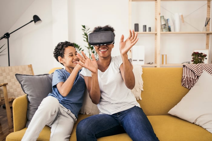 Adult wearing a virtual reality headset, having fun on the couch with a child.