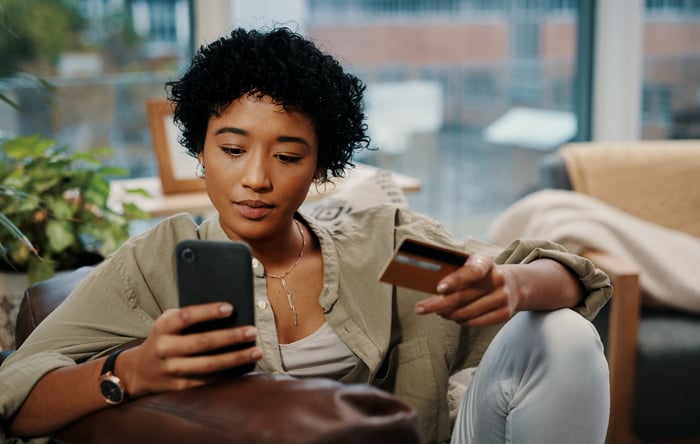 Person sitting in a chair while inputting their credit card details while holding a mobile device.