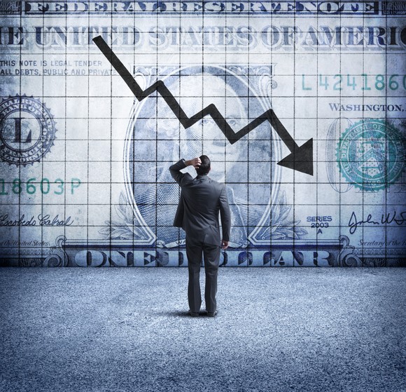 A person watching an arrow following a downward pattern along a dollar bill.