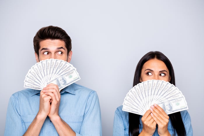 A man and a woman look at each other and hold up a fan made of money