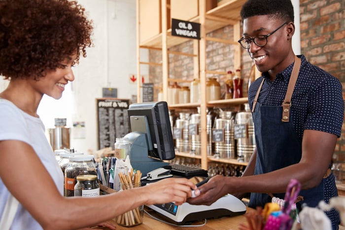 A customer making a contactless payment to the merchant in a small goods store.