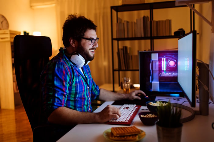 A person smiling while seated at their desk playing games on a computer.