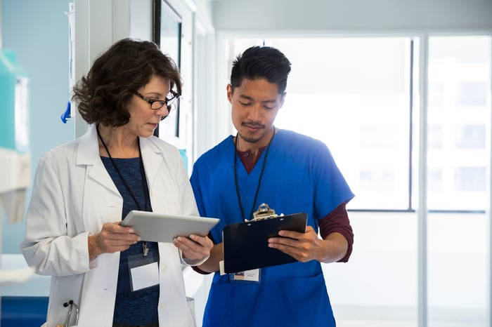 Two health professionals looking at a tablet and a clipboard.