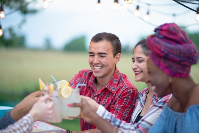 A group of people sitting outside and raising glasses of lemonade.