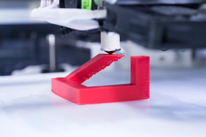 Close-up of a 3D printer producing a red plastic object.