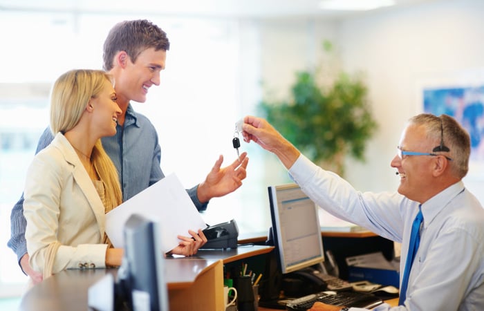 Couple accepting car keys from a rental salesman at a desk.