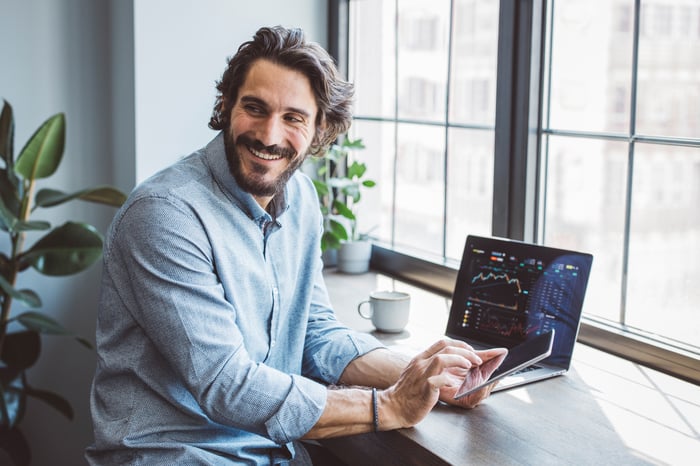 Person smiling holding a phone while looking away from their computer.