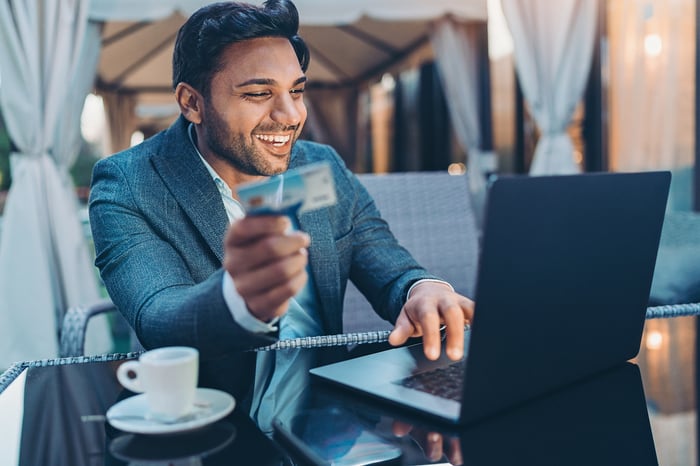 A smiling shopper holding a credit card makes purchases on a laptop computer.