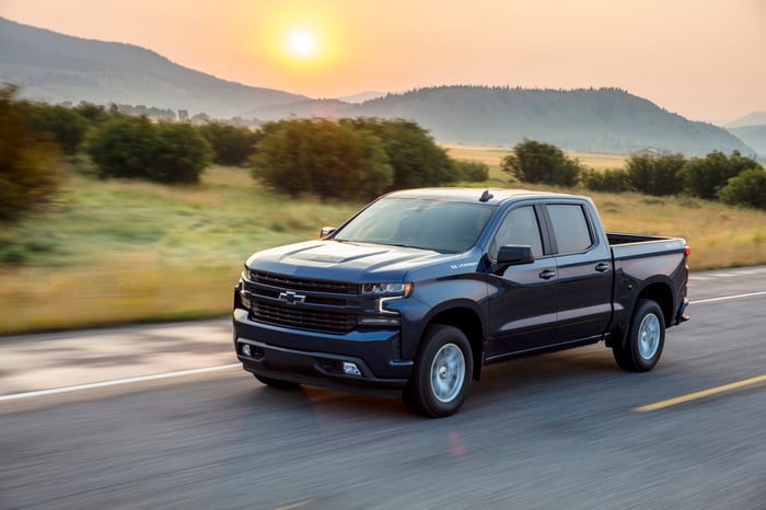 A dark-colored Chevy Silverado driving on a rural road.