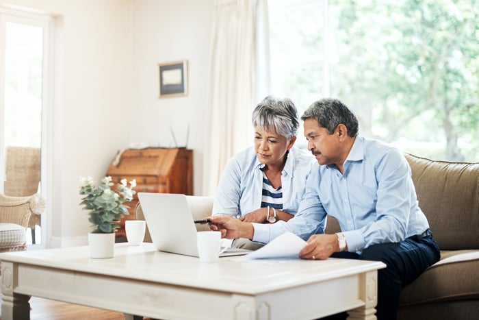 Two older people sitting on a couch looking at a laptop