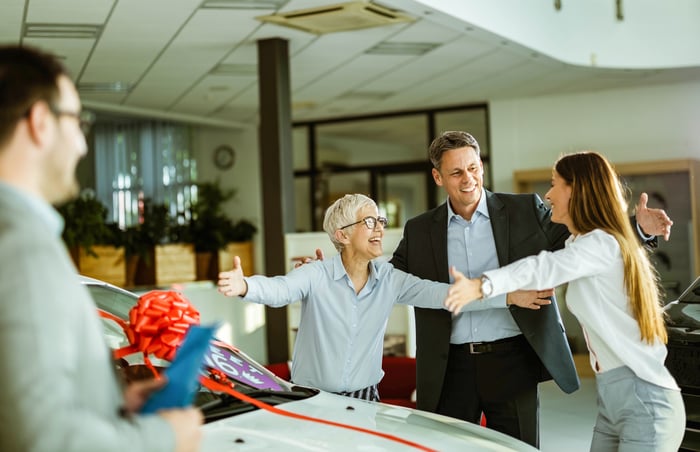 People about to hug near a car with a red bow on it.