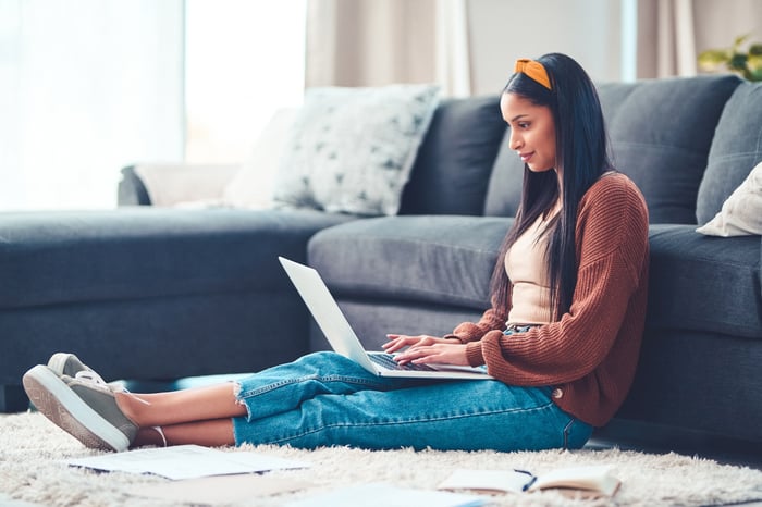 Smiling person using laptop surrounded by paperwork.