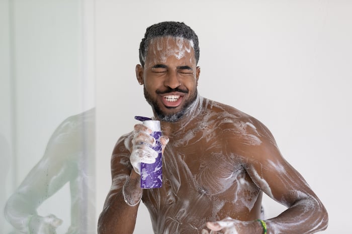 A soapy person in the shower singing into a shampoo bottle.