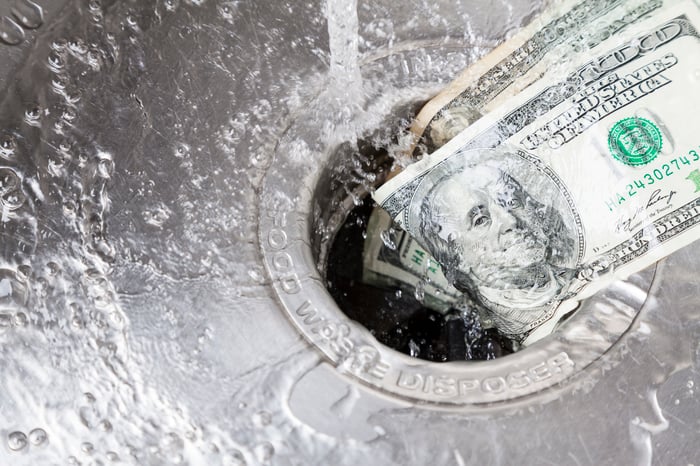 Hundred-dollar bills being washed down a drain.