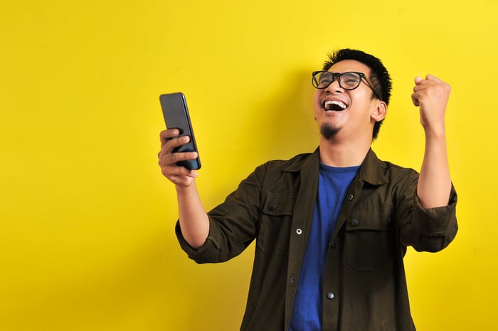 A person holding a phone while looking up and cheering.
