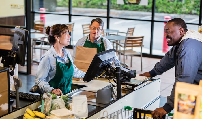 A cashier checking out a customer at a grocery store while another employee bags the items. 