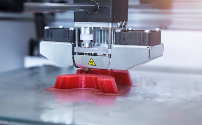 Close-up of a 3D printer producing a red plastic object.