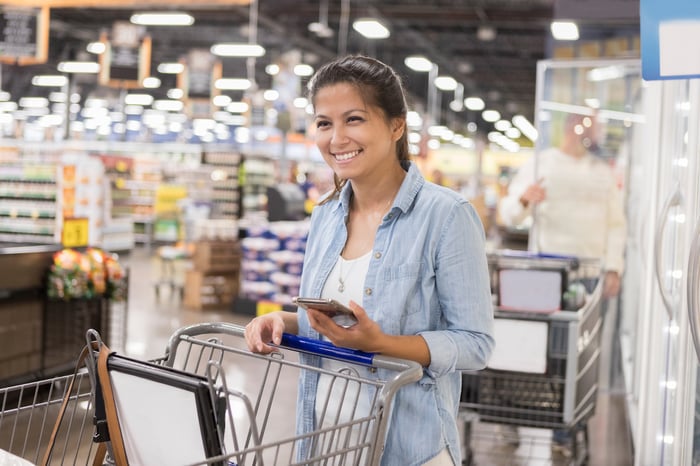 A smiling person pushes a shopping cart in a large store.
