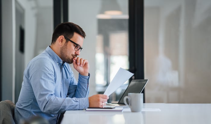 A person at a laptop holding a document.