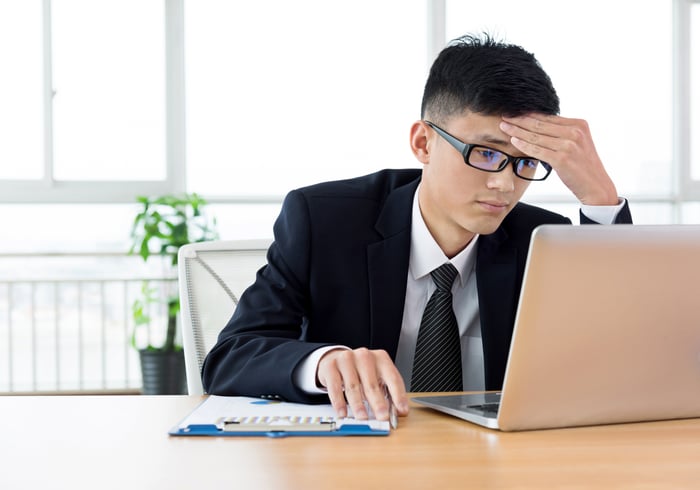 A person in a business suit with a serious expression at a laptop.