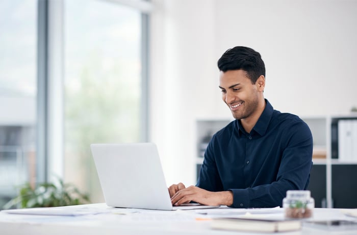 A smiling person at a laptop.