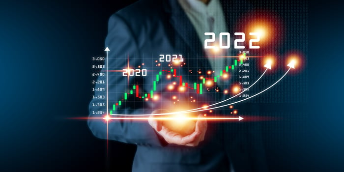 Man in business suit holds glowing stock chart showing arrows rising in 2022.