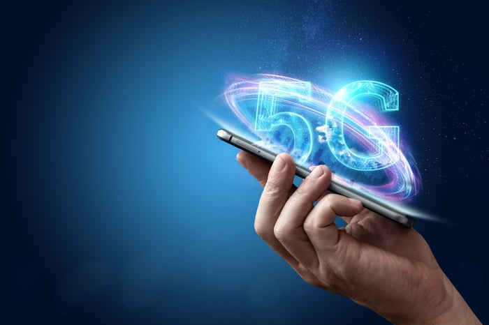 A hand holding a mobile device with 5G written above it.