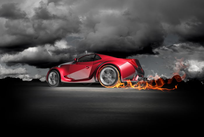 Futuristic red sports car burning up the track with flames at wheels under a black and white sky.