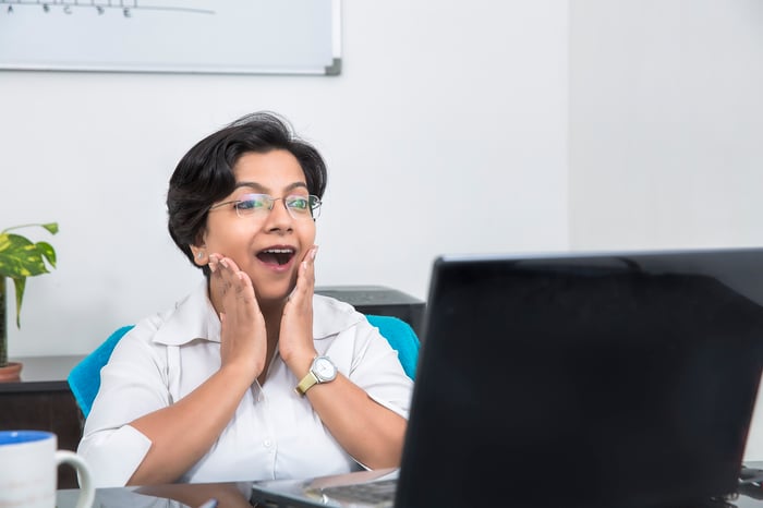 A person places hands on their cheeks in surprise while looking at computer screen.