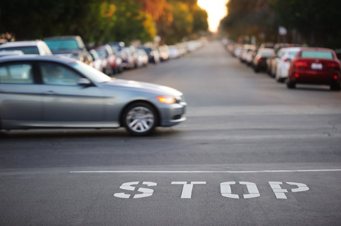 Car traveling through an intersection past a painted STOP on the pavement.