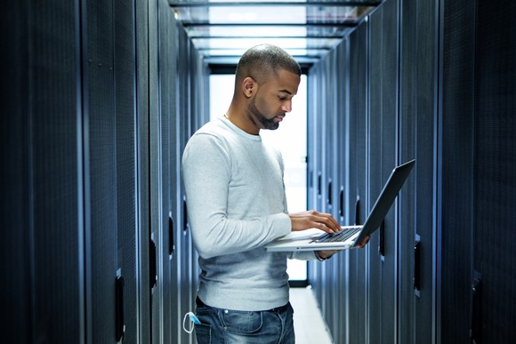Person with laptop computer in front of bank of servers