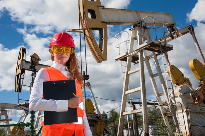 A person in protective gear in front of oil wells.