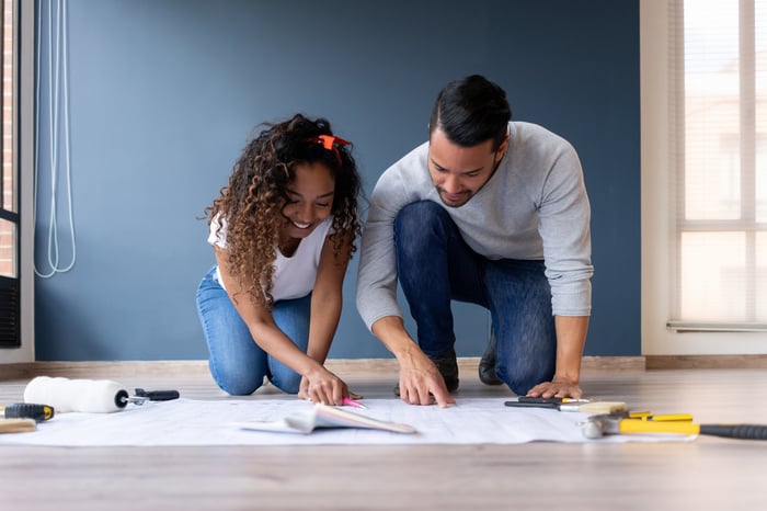 Two people kneeling over a large, white paper on the floor.