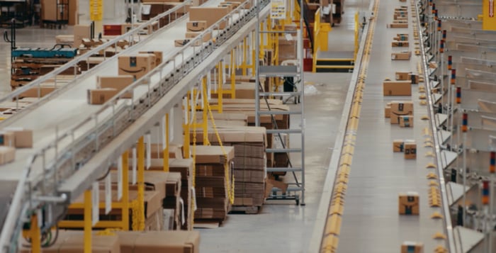 Amazon packages moving on conveyor belts in a distribution center.