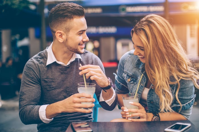 Two people drinking glasses of lemonade sitting at an outside table.