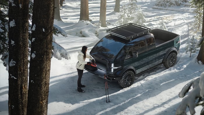 A person standing next to a Canoo vehicle in the snow. 